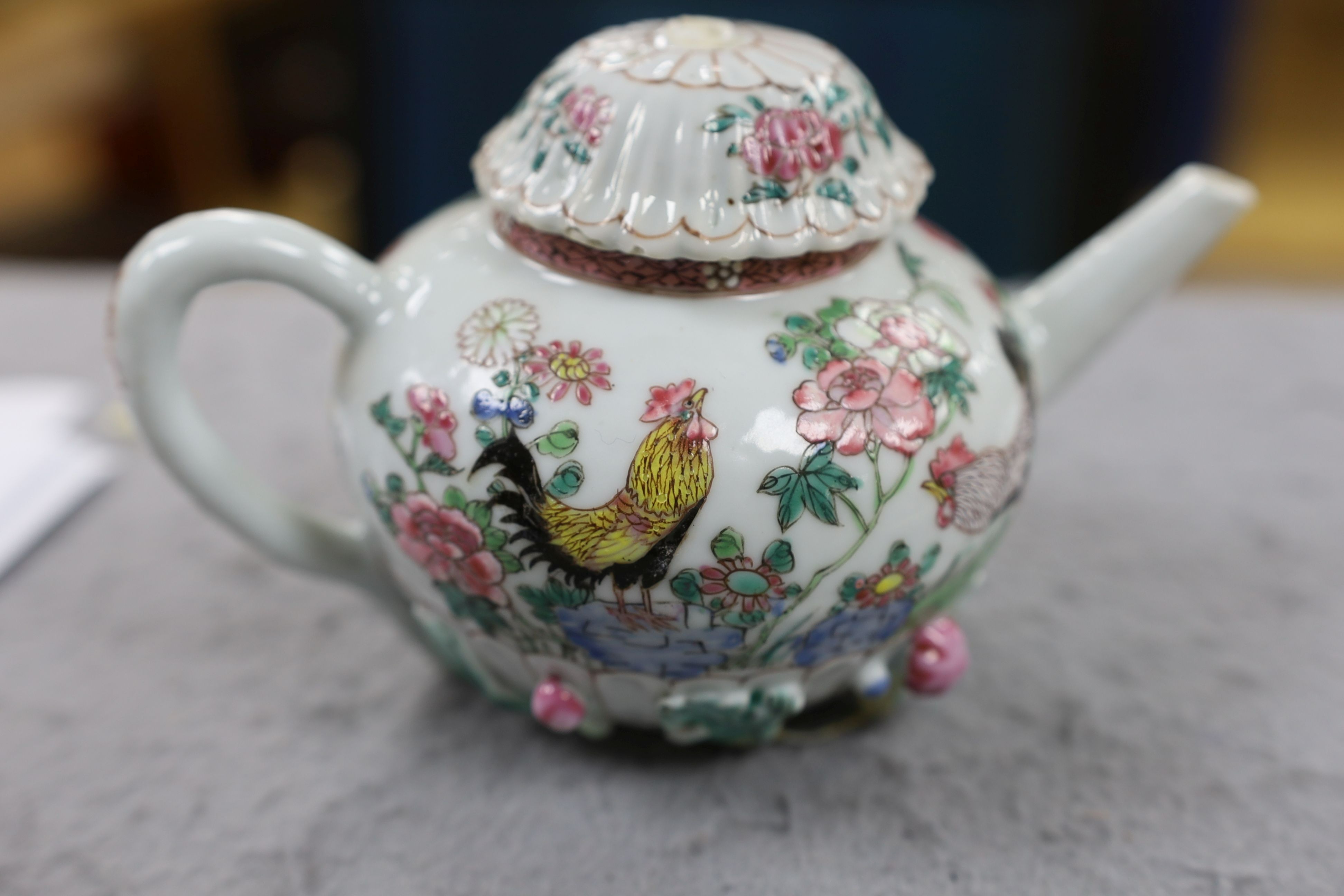 A Chinese famille rose chrysanthemum moulded teapot, early Qianlong period, painted with a cockerel amongst flowers, on a cage work base, 10 cms high